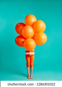 Girl holding orange balloons in front on blue background. Full length of small girl child with bunch of helium balloons.