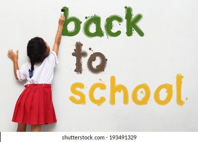girl holding a paint brush painting back to school text on wall