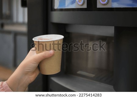 Girl holding paper cup with drink near coffee and hot beverage vending machine, closeup. Space for text
