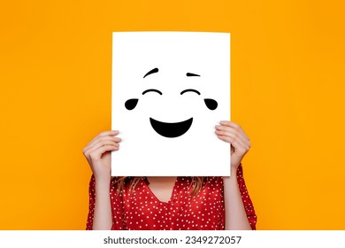 Girl holding a paper poster with a happy laughing smiley isolated over orange background. Humor concept
