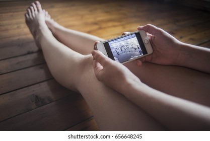 Girl Holding The Phone In Hand Against The Bare Feet And The Wooden Floor