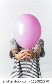 Girl holding pink balloon in front of her face on white brick wall background