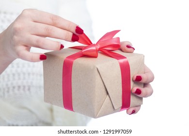 girl holding a present in hands, woman pulling ribbon opening the box wrapped in craftpaper on white isolated background, concept winter holiday - Shutterstock ID 1291997059