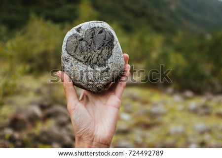 a girl holding a rock with a heart at the mountains background