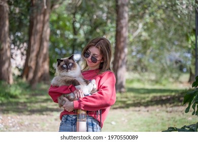 Girl holding seal point ragdoll cat outdoors in a park