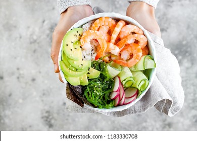 Girl holding shrimp poke bowl with seaweed, avocado, cucumber, radish, sesame seeds. 