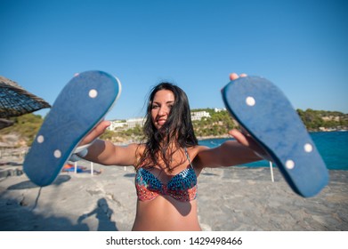 The Girl Is Holding Slippers. Flip Flops On The Beach.