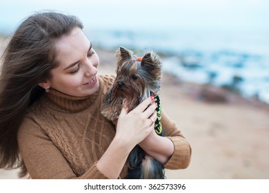 Girl Holding A Small Dog In Her Arms On The Beach