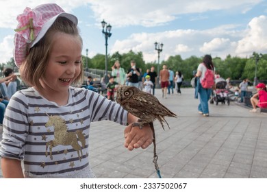 Girl holding small owl while standing in park against sky
