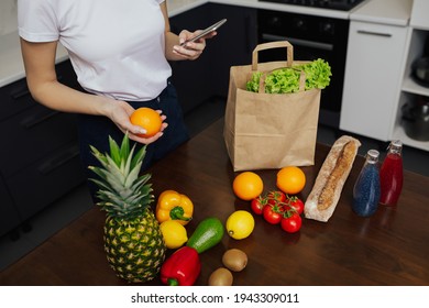 Girl Holding Smart Phone While Unpacking The Food After Shopping.