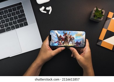 Girl holding a smartphone with LOL League of Legends Wild Rift game app on the screen on black background table. Office environment. Rio de Janeiro, RJ, Brazil. February 2022.