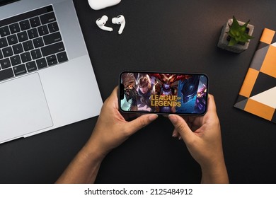 Girl holding a smartphone with LOL League of Legends game app on the screen on black background table. Office environment. Rio de Janeiro, RJ, Brazil. February 2022.