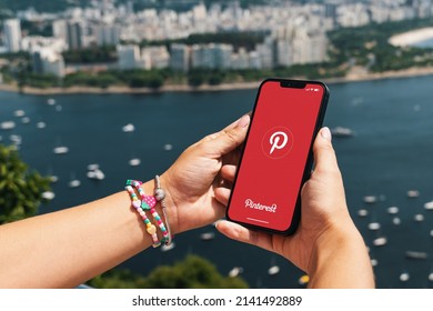 Girl Holding Smartphone With Pinterest App On Screen. City And Bay With Some Boats In The Background. Rio De Janeiro, RJ, Brazil. March 2022.