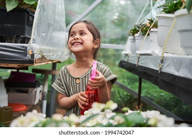 Girl Holding Spray Bottle With Water And Laughing While Watering Flowers At The Garden