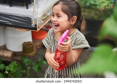 Girl Holding Spray Bottle With Water And Laughing While Watering Flowers