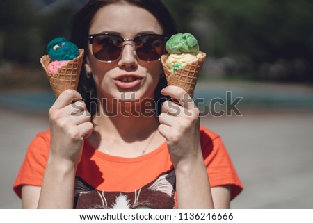 A girl holding two-tone ice-cream cone showed up under blue sky in hot summer day on vacation. Strawberry and orange flavor soft-cream cone for refreshing.