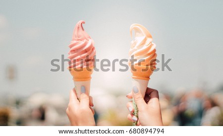 A girl holding two-tone ice-cream cone showed up under blue sky in hot summer day on vacation. Strawberry and orange flavor soft-cream cone for refreshing.