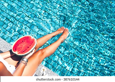 Girl holding watermelon in the blue pool, slim legs, instagram style. Tropical fruit diet. Summer holiday idyllic.