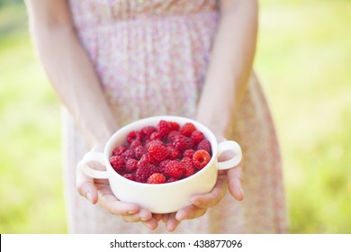 Girl holding a white plate with ripe raspberries.