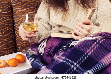 Girl Holding Wineglass With White Wine And Old Book. Woman Reading Book And Drinking Wine At Home. Cozy Christmas Atmosphere.