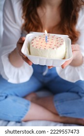 A girl holds a bento cake in her hands with a burning candle in the middle. Vertical photo