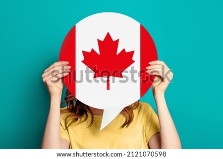 girl holds blank white speech bubble with canadian flag isolated on blue background. Invitation to study in Canada concept