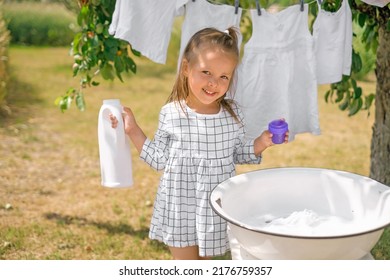 Girl holds bottle of liquid laundry detergent in hands, standing at basin for hand washing clothes. Snow-white baby underwear on clothesline. Advertising of eco friendly hypoallergenic detergents - Shutterstock ID 2176759357