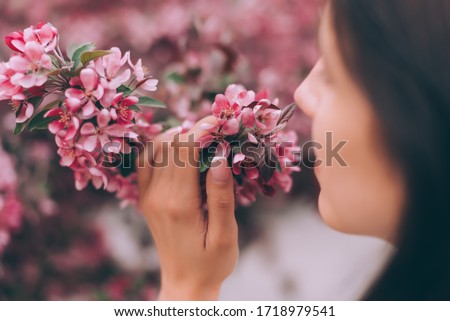 Girl holds a branch of blossoming spring flowers in hands. Close up of beautiful female hands holding a branch of blossoming fruit tree. Delicate spring background. Pink background.