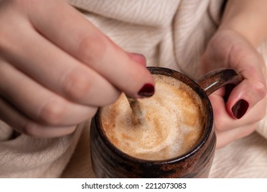 A Girl Holds Cappuccino Coffee In A Ceramic Cup. Warm Blanket And Ceramic Cup In Hand. Milk Foam, Texture. Autumn Cold, Warm Up With A Warm Drink And Under A Blanket.