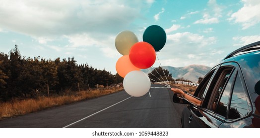 Girl Holds Colorful Balloons Out Of Car Window. Freedom, Happiness And Celebration Concept. Letterbox Format.