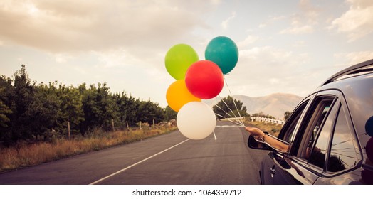 Girl holds colorful balloons out of car window. Freedom, happiness and celebration concept. Letterbox format.