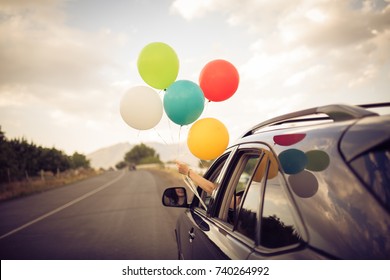 Girl holds colorful balloons out from the window of the car. Freedom, happiness and celebration concept.