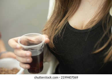 Girl Holds Glass With Drink In Her Hand. Girl Drinking Tea Outside. Black T-shirt And Long Hair. Hot Drink In Plastic Cup.