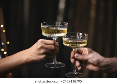 A girl holds glasses of champagne in her hands, cheers with a man. Le coupe cocktail glasses. Celebrates the New Year or a corporate holiday. Disco or retro style. They bump glasses, clink glasses - Powered by Shutterstock