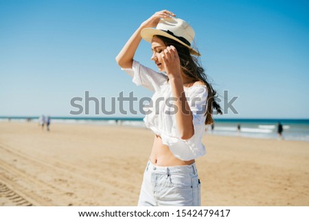 girl holds a hat from the wind on the beach