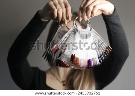 The girl holds in her hands a palette of samples of colored nail polishes. The face is not visible. Gray background. Nail color polish display. Choose the color of nail polish.
