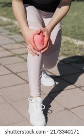 The Girl Holds An Injured Knee Joint In Her Hands. Injury While Running Outdoors.