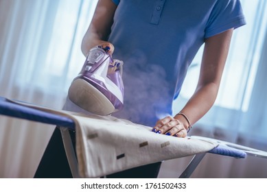 The Girl Holds An Iron On An Ironing Board With A Ferry And Irons Things. Cleaning Service Of The Apartment. House