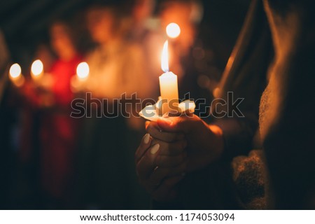 a girl holds a lighted candle in her hands, a religious tradition, a symbol of the Christian faith, a wax candle burns with an even flame, blow out a candle, a smoke from an extinguished wick

