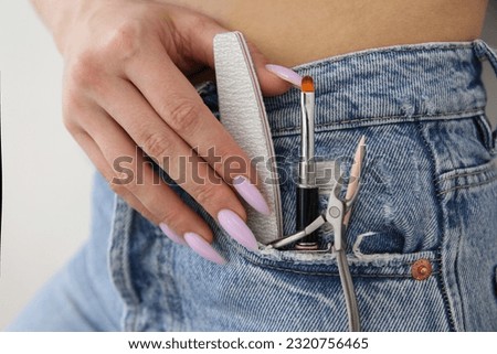 The girl holds manicure tools in her jeans pocket. Style. The process of doing a manicure in the salon. Polishing nails, cuticles. Nail service, cosmetic procedures, nail business