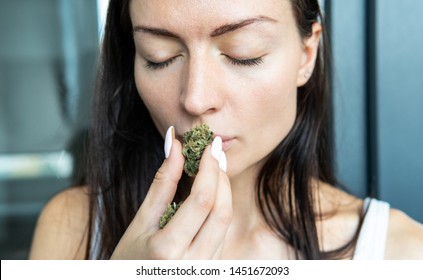 the girl holds a marijuana bud in her hands and sniffs her smell in front of her face.