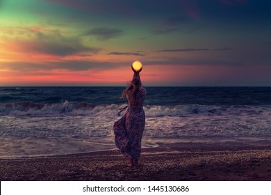 The girl holds the moon in her hands. Beautiful sunset on the sea. Dreams come true. Everything is possible.