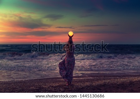 The girl holds the moon in her hands. Beautiful sunset on the sea. Dreams come true. Everything is possible.
