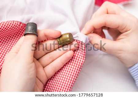 The girl holds a needle and two thimbles in her hands. Vintage thimble. Sewing. Against the background of pink and white fabric.