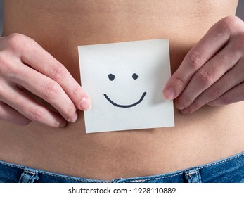 The girl holds a paper sticker with a smiley face in front of her bare stomach. Concept of pregnancy and motherhood