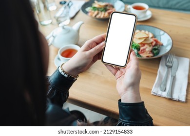 The girl holds a phone in her hands with a blank isolated screen on the background of food in a restaurant. Place for your menu or review.. - Shutterstock ID 2129154833