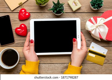Girl holds tablet, chooses gifts, makes purchase, cup of coffee, debit card, two hearts on wooden table Top view Flat lay Holiday shopping list, Happy Valentine's day, online shop concept Mock up - Powered by Shutterstock