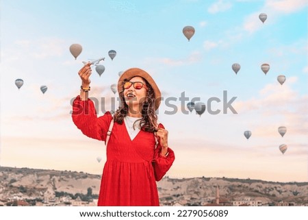 Girl holds a toy airplane with Cappadocia's hot air balloons in the background, representing air transport and travel concept.