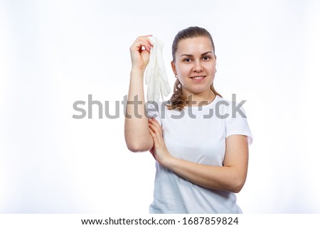 The girl holds white medical gloves in her hands. Protection against germs and the virus. She is in a white T-shirt on a white background.
