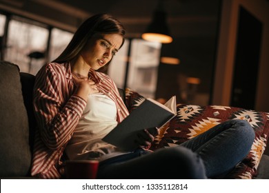 Girl at home studying. Teen reading a book on the couch. 